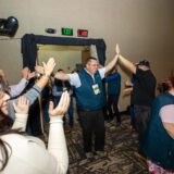 A group of people in red lanyards smile as they play the drums.
